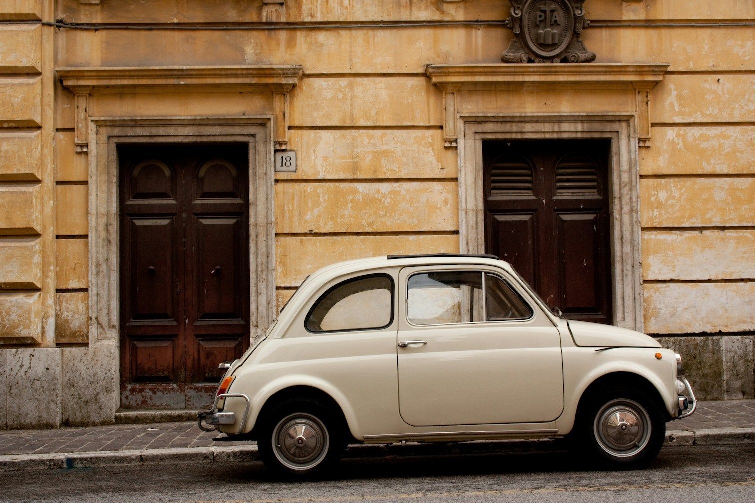 Small white Fiat parked along street in front of two doors on European street